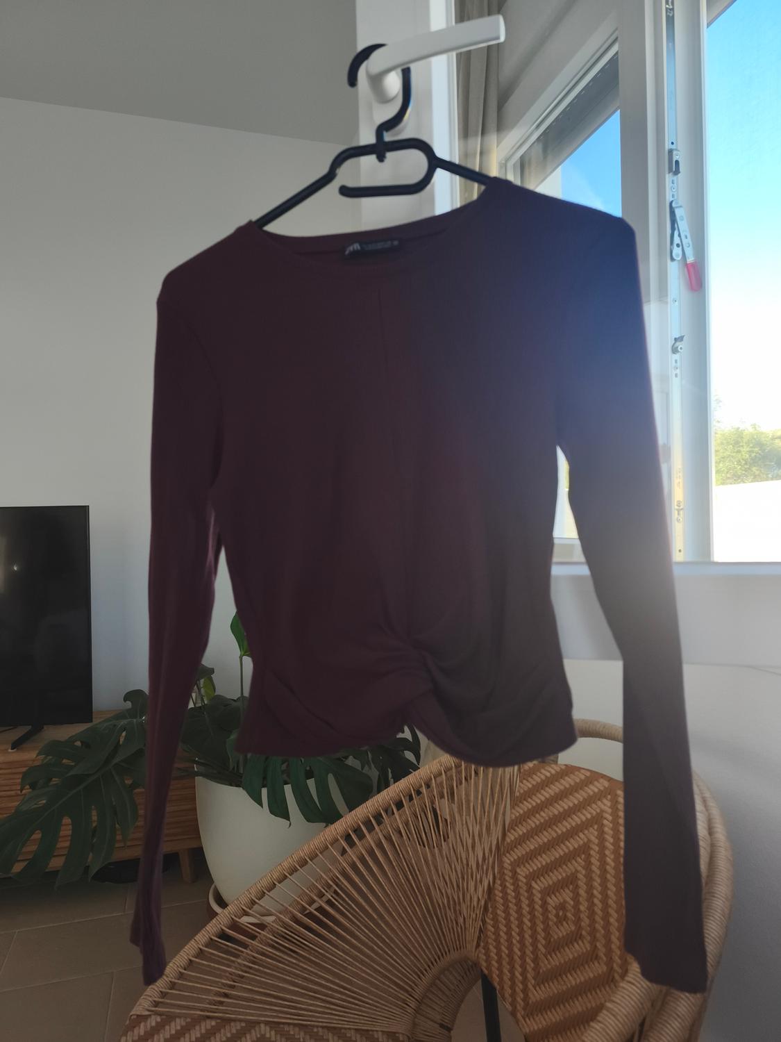 Dark purple jumper hanging on a black hanger, on a wicker chair next to a window with natural light.