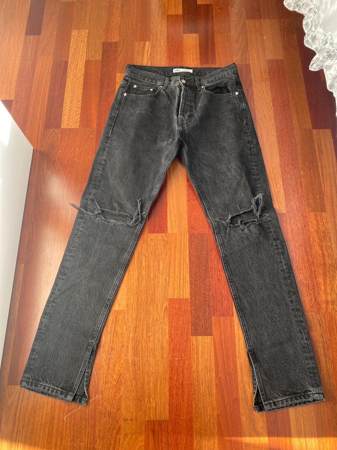 Front view of worn black trousers with front pockets and ripped knees.