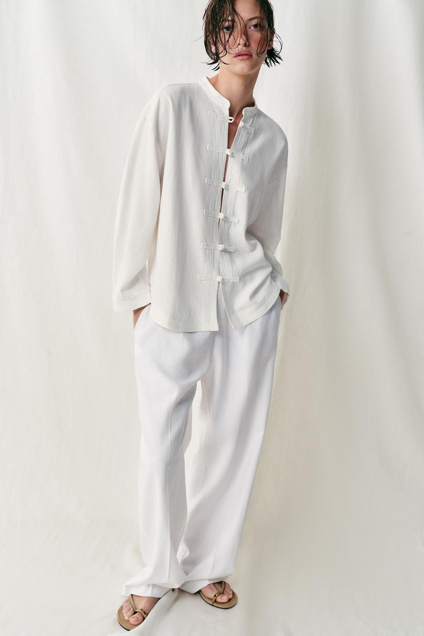 White long-sleeved loose shirt set with a round neck and toggle front closure, and white wide-leg pants.