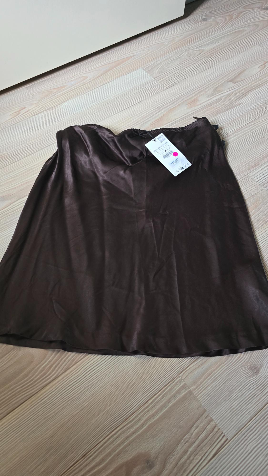 Brown soft fabric skirt on a light wooden floor, with a white label visible in the top right corner.