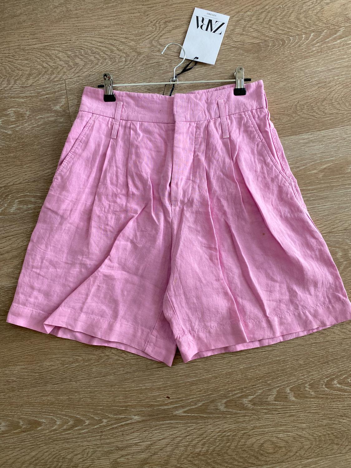 Light pink shorts hanging on a hanger against a light wooden background. Visible tag with the text "ZARA".