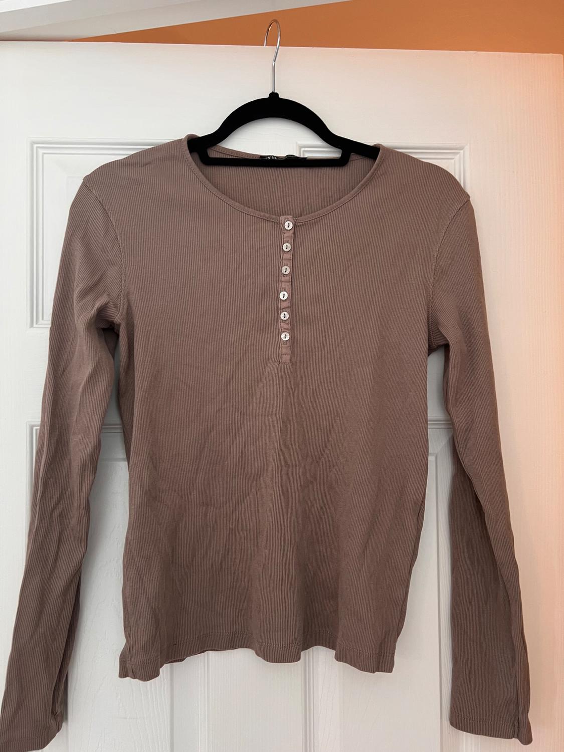 Brown long-sleeved ribbed top with buttons, hanging on a black hanger on a white door. Relaxed and casual atmosphere.