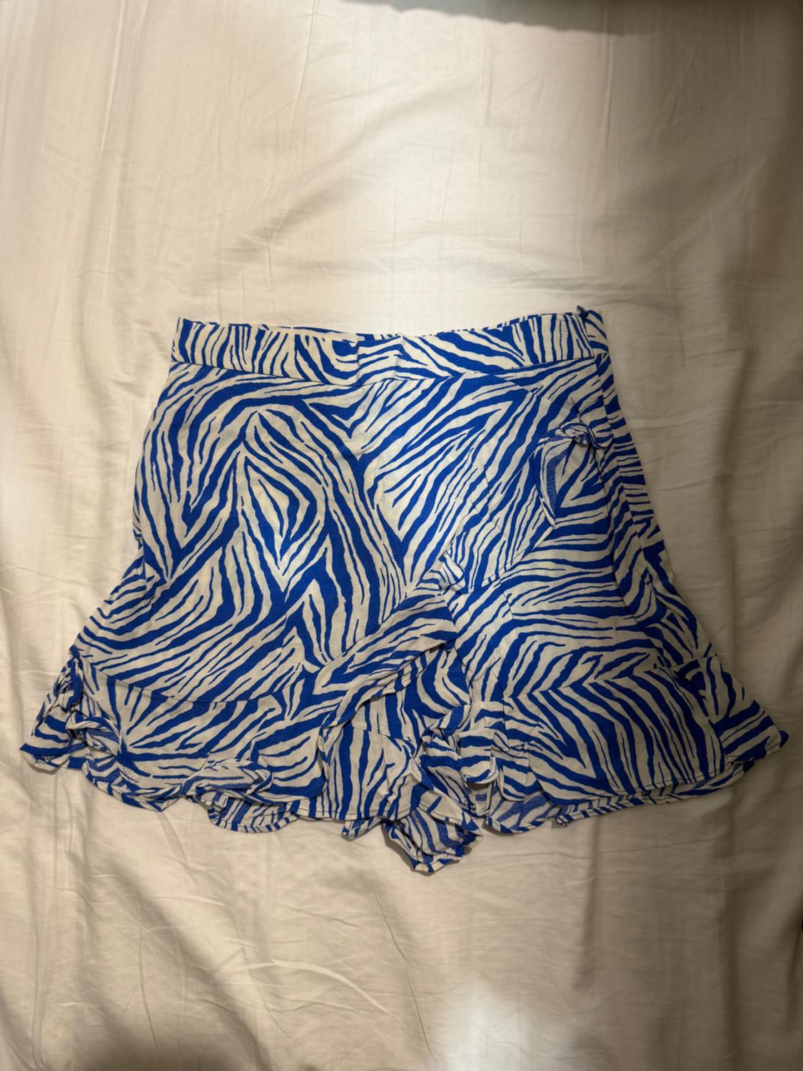 Blue and white striped shorts on a white bed. Lightweight fabric with frills on the hem.