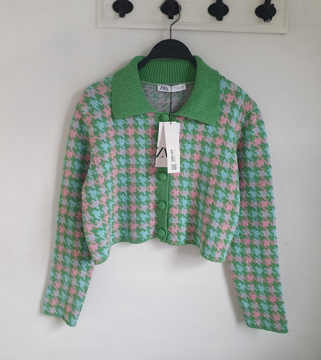 Green and pink knitted cardigan with buttons and collar, hanging on a black hanger. Visible label with Zara logo.