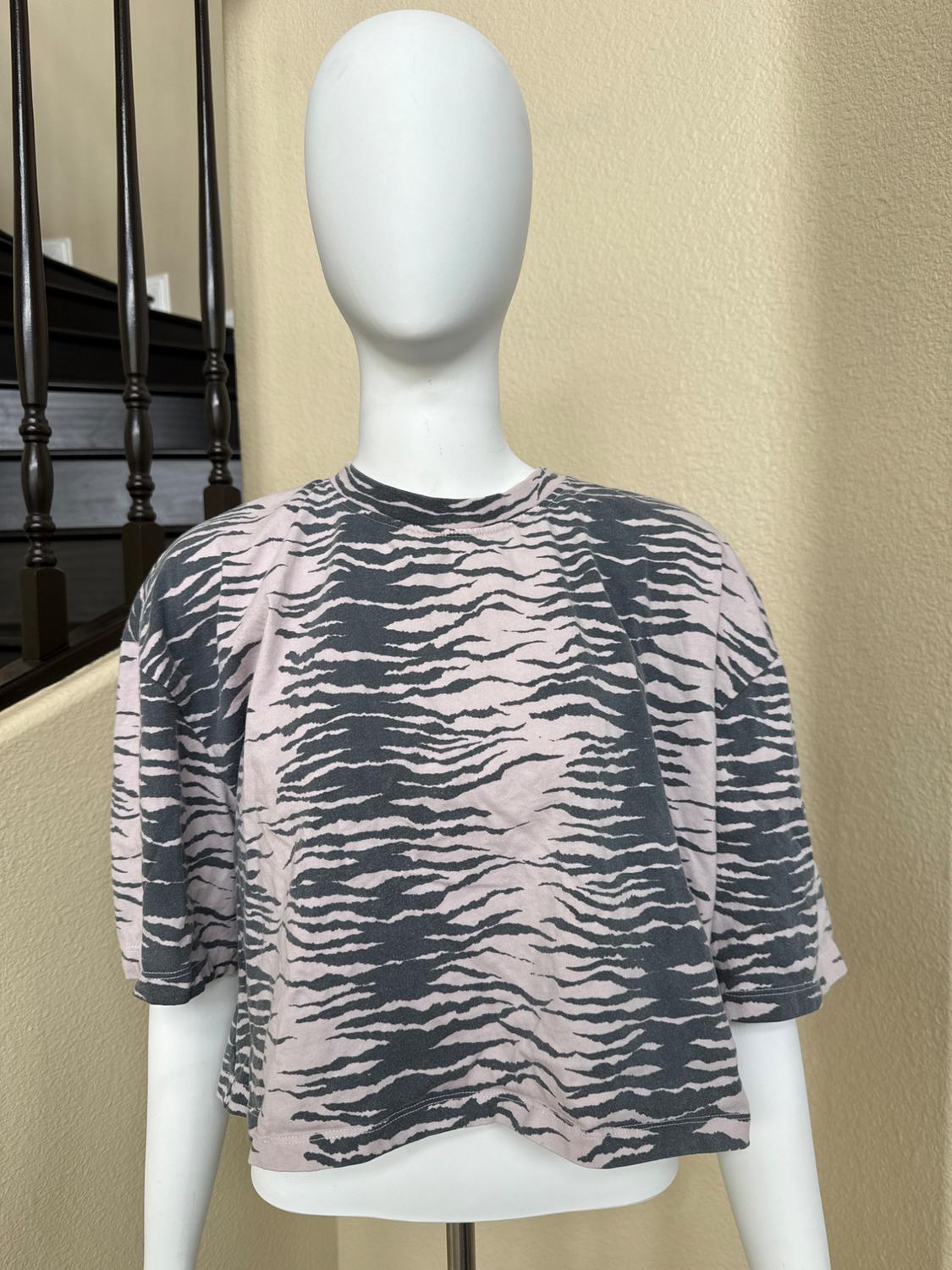 Mannequin wearing a loose-fitting short-sleeved cropped t-shirt with a dark striped animal print on a light background, in an interior with a staircase.