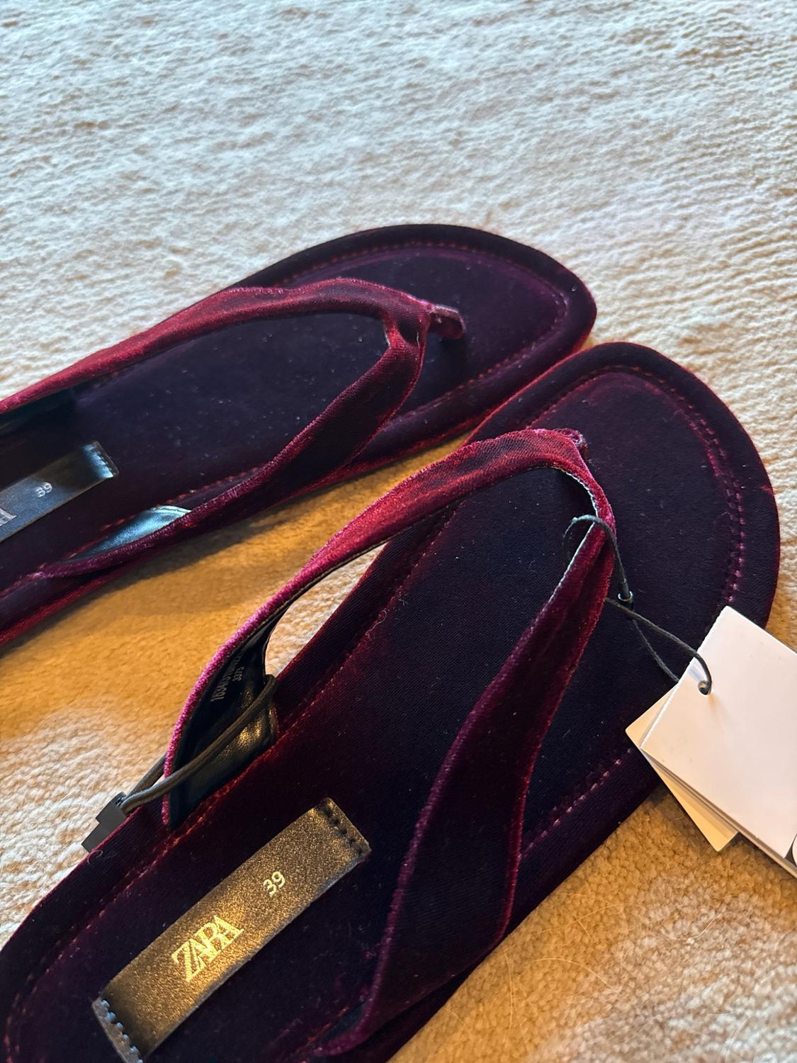 Close-up of maroon velvet toe-post sandals on a light-coloured carpet. The black insole reads ZARA 39.