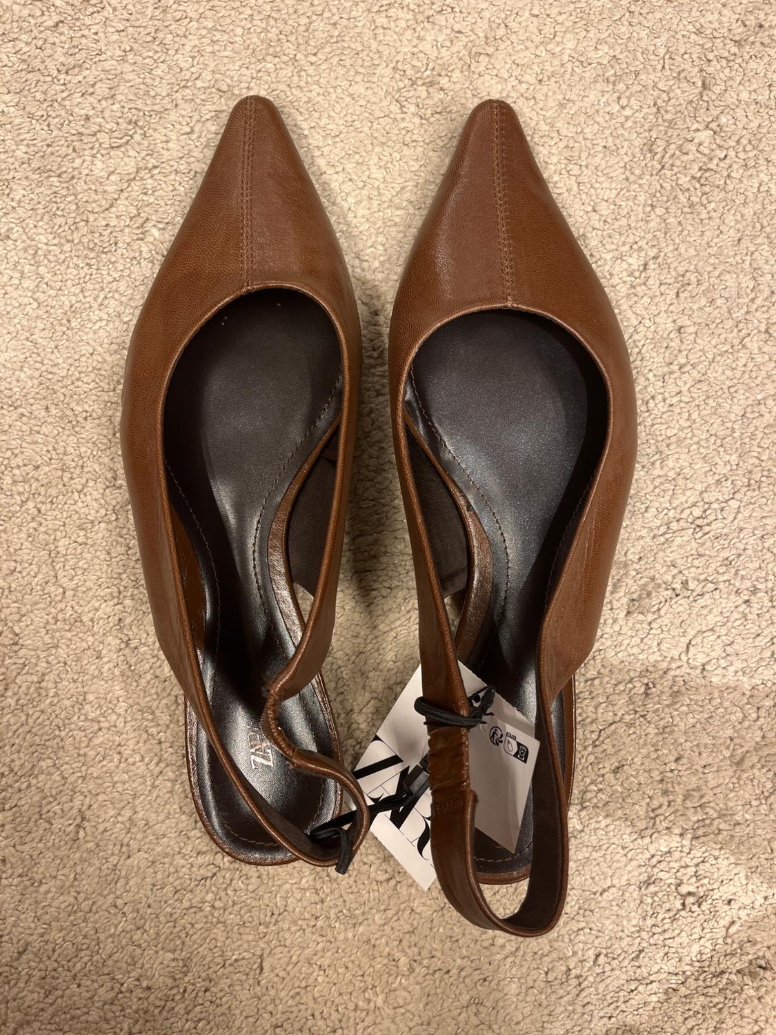 Brown pointed-toe shoes with straps, seen from above on a beige carpet. Label visible on one of the shoes.