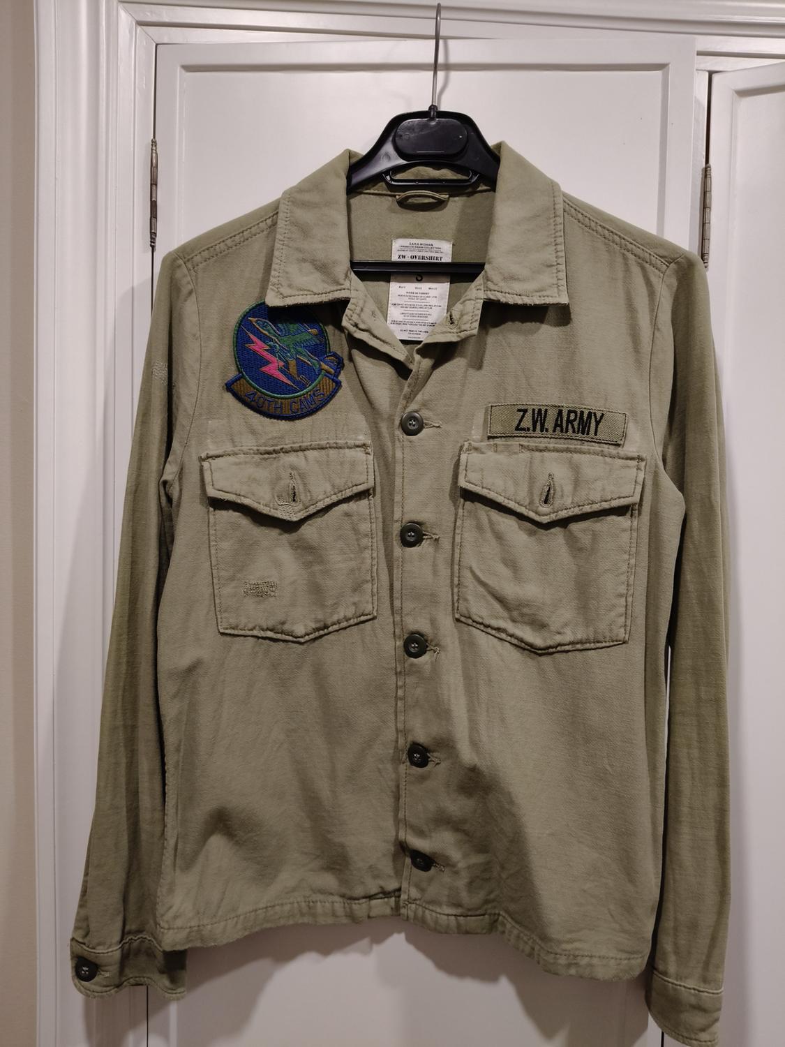 Front view of a green jacket with front pockets, black buttons, 'Z.W. ARMY' text and a colourful patch on the chest.