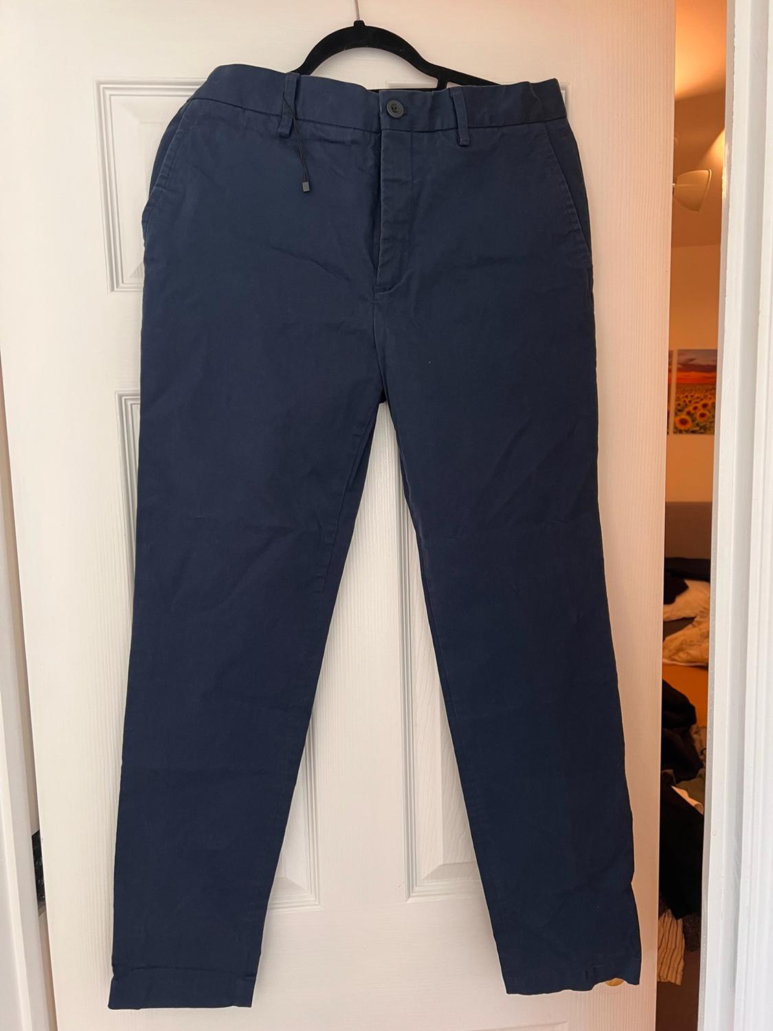 Navy blue trousers hanging on a black hanger over an ajar white door, revealing the interior of a room in the background.