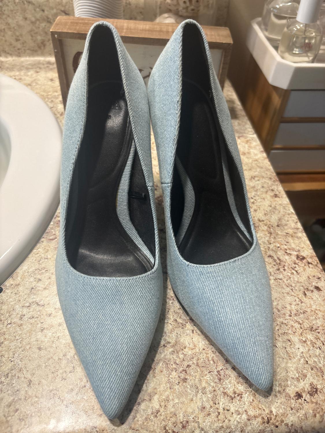 Light blue fabric high heels with a pointed toe, placed on a marble countertop in a bathroom setting.