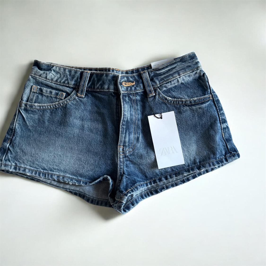Blue denim shorts with a white hanging tag that says "ZARA", on a white background.