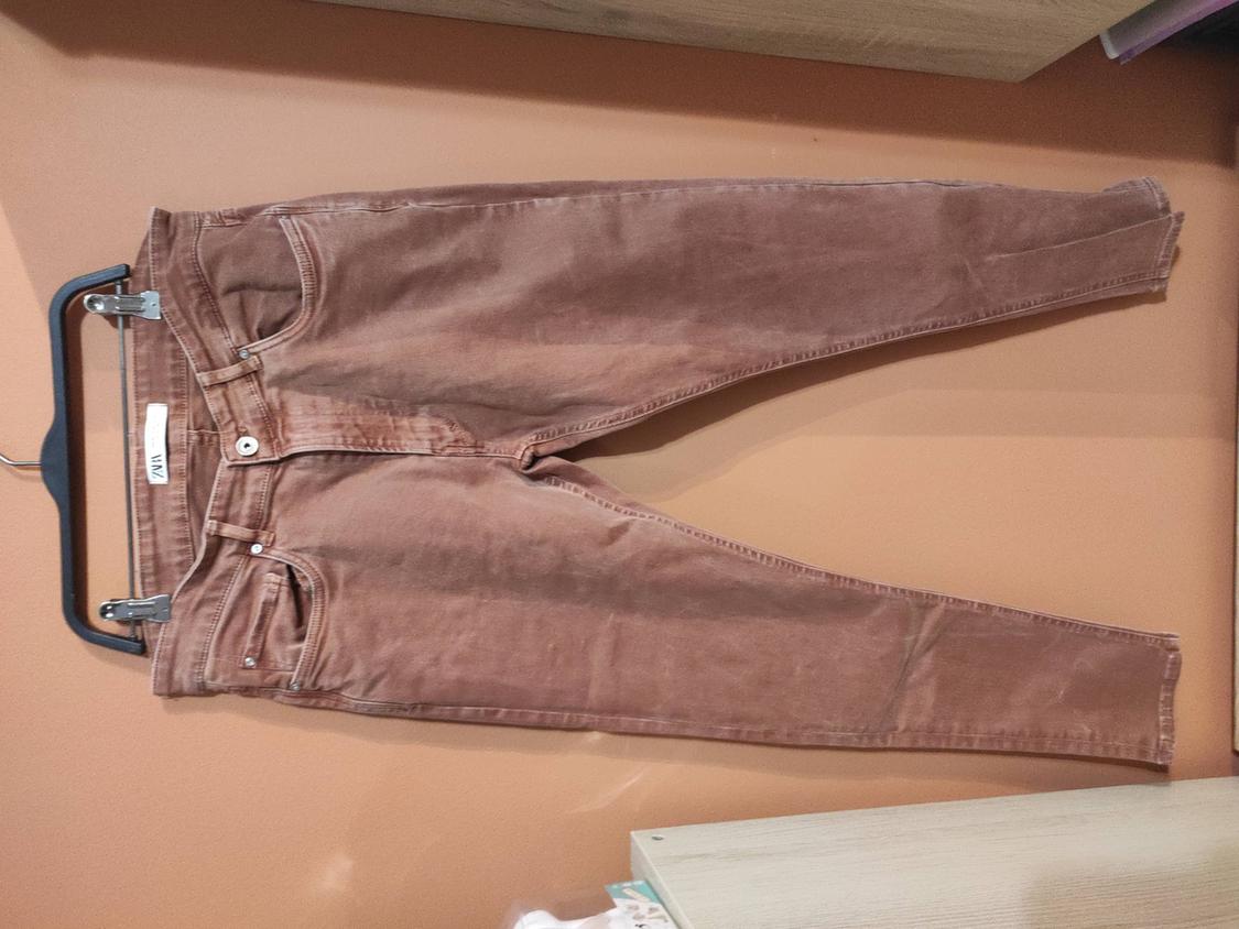 Brown trousers hanging on a black hanger against a beige wall. Visible label with the text "ZARA".