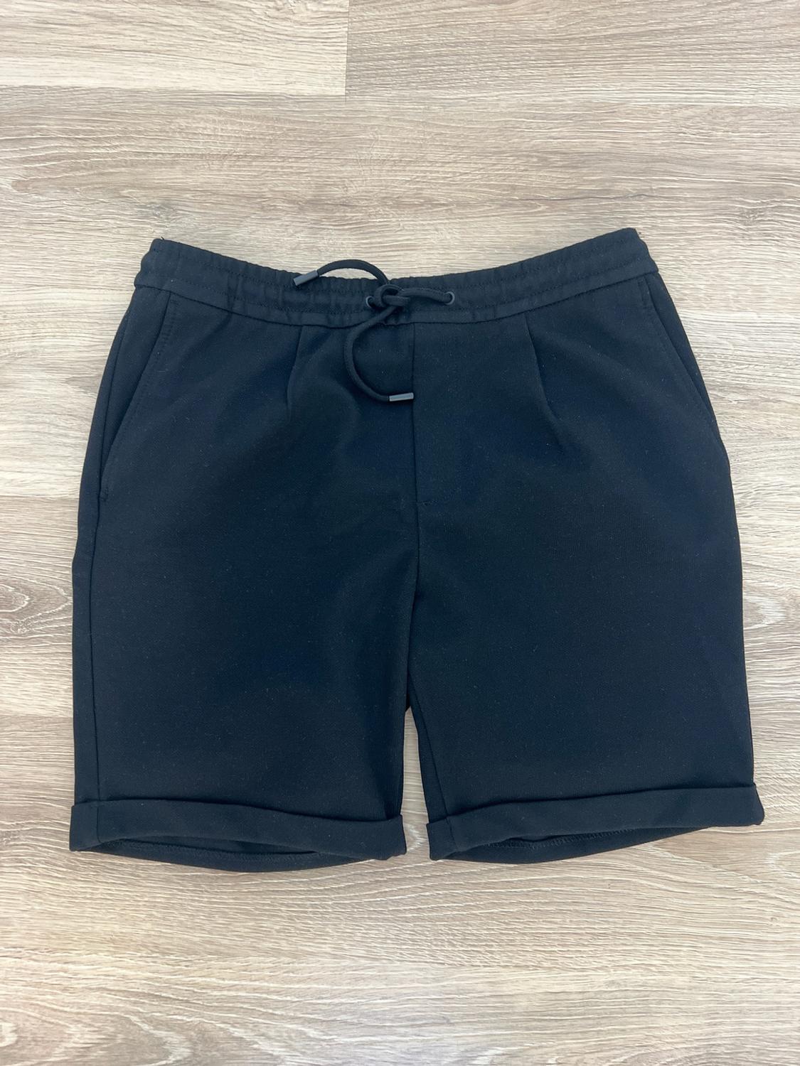 Casual black shorts with an elasticated waist, adjustable drawstring and turn-up hems, laid out on a light wood background.