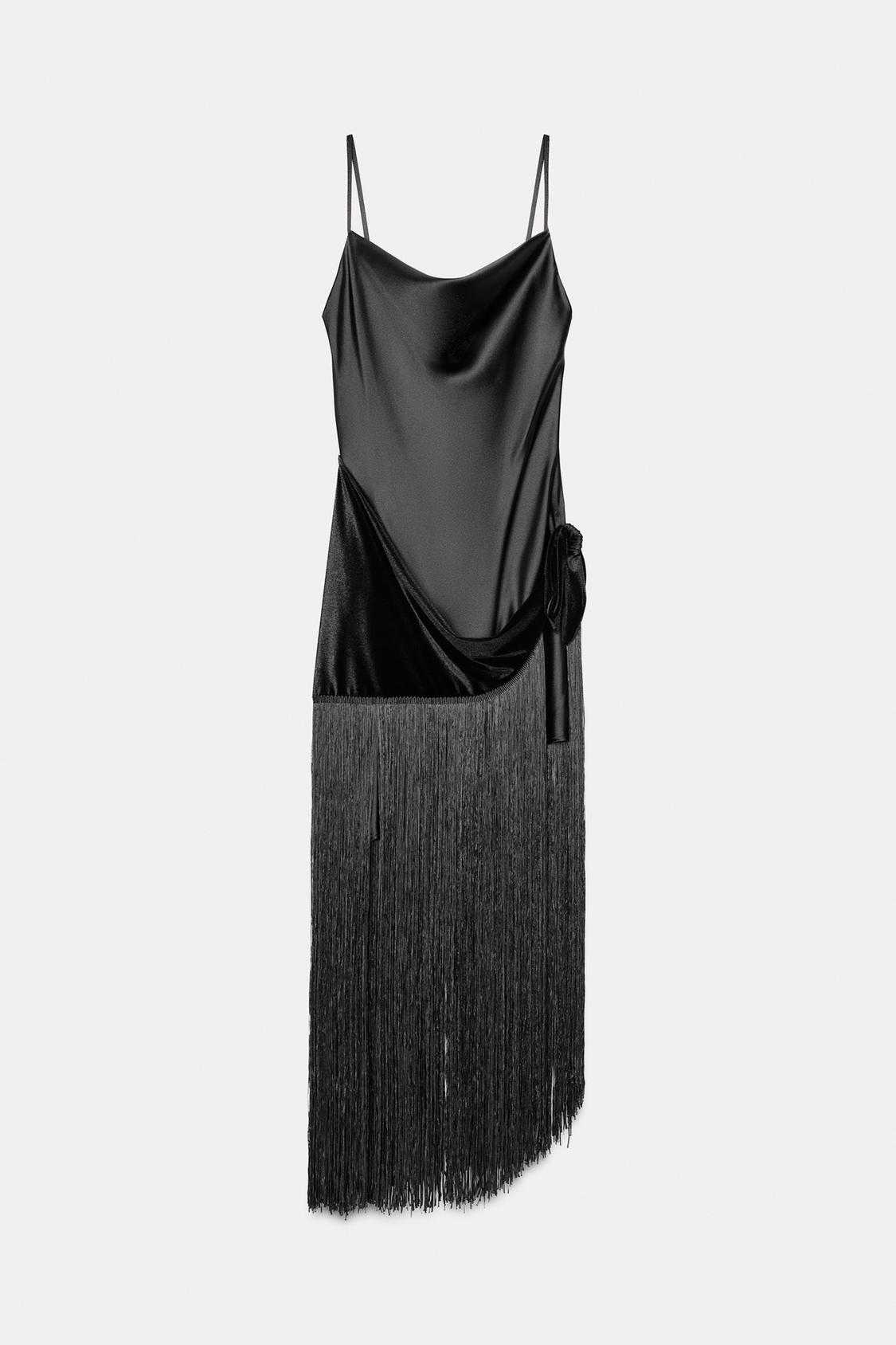 Front view of a black dress with a flowing neckline, thin straps, velvet sarong detail, and long fringes on the hem.
