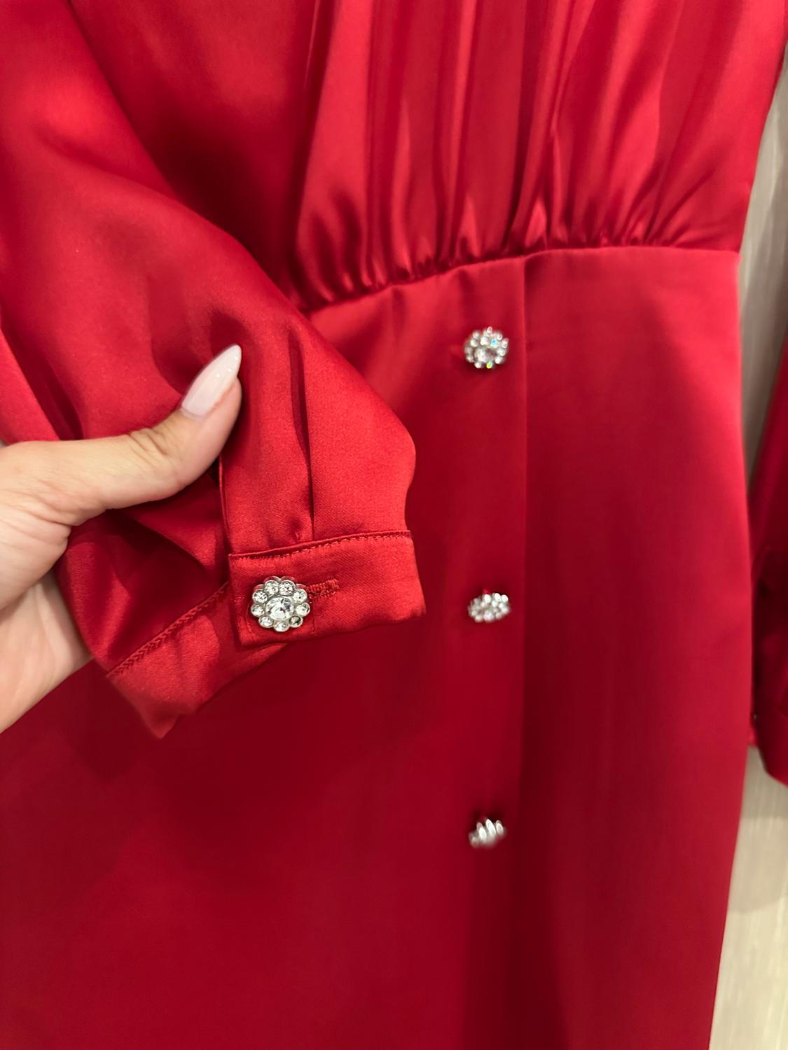 Here is a rephrased version that maintains the same meaning and context, without using any of the prohibited words: "Detailed view of a red satin garment. A hand is holding the sleeve cuff, revealing shimmering flower-shaped buttons."