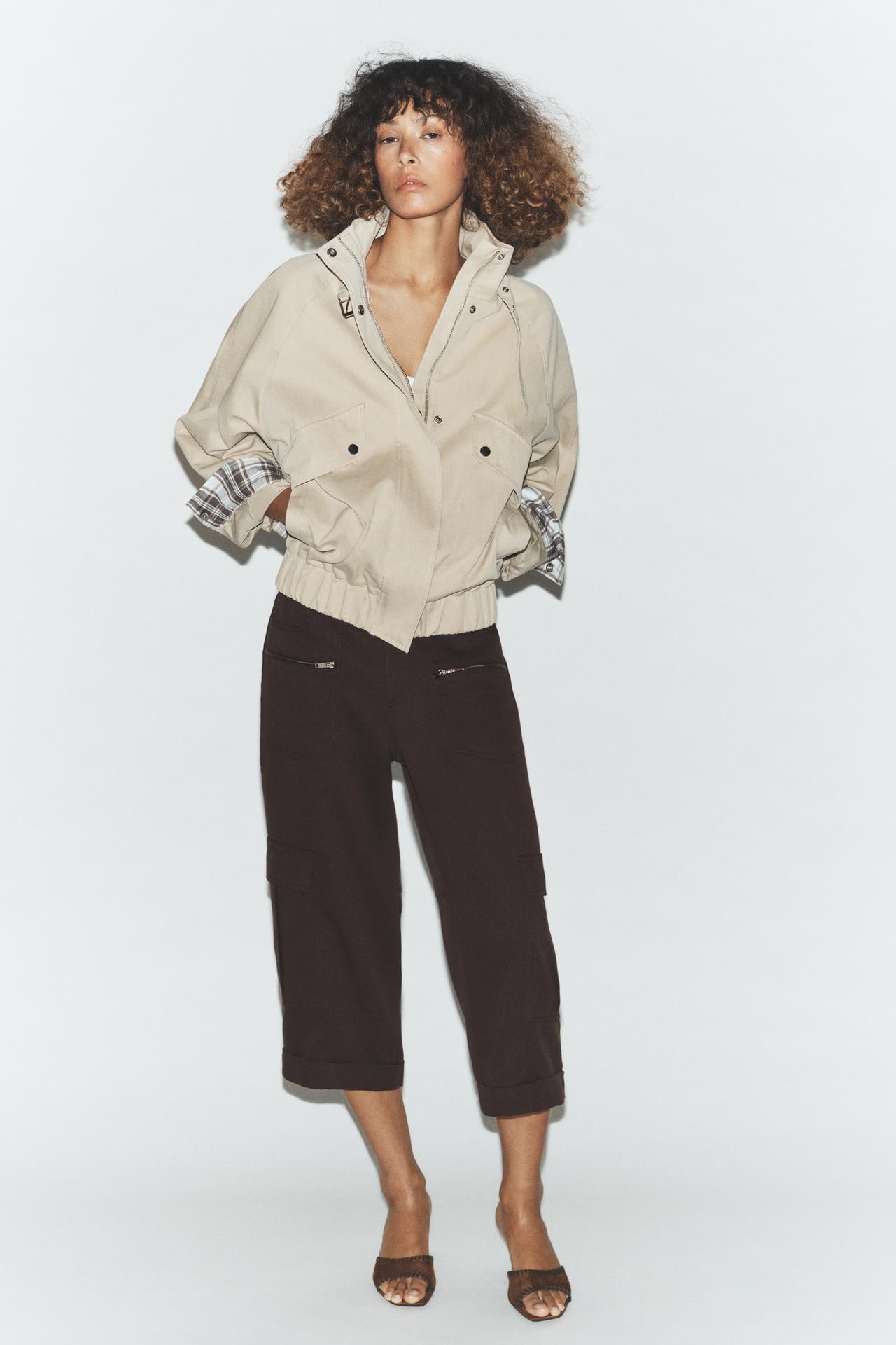 Beige jacket set with front pockets and dark pants with zippers and side pockets.