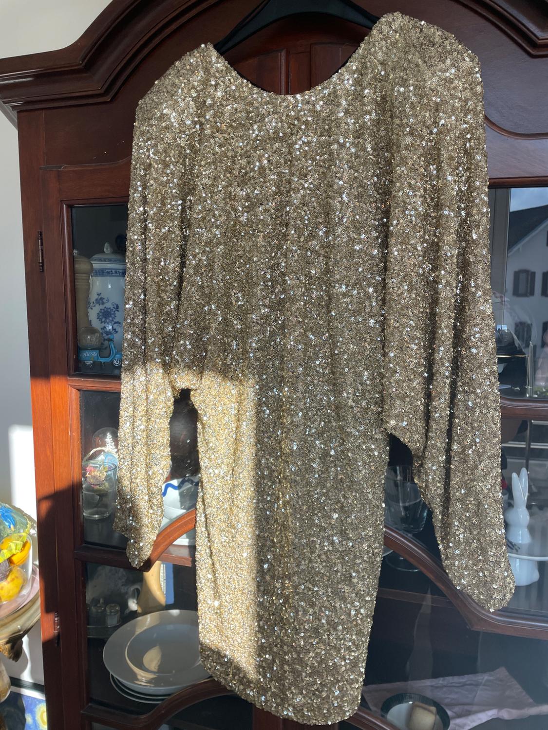 Gold sequined dress hanging on a hanger in front of a wooden cabinet with crockery inside.