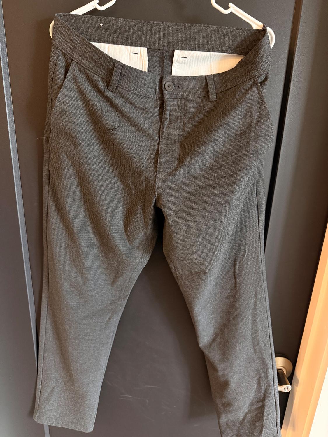 Gray pants hanging on a white hanger over a dark door. Classic design with side pockets and button closure.