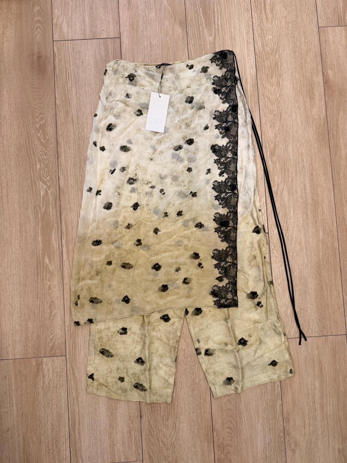 Beige ombré set with black print, side lace and ZARA label, laid out on a wooden plank floor.