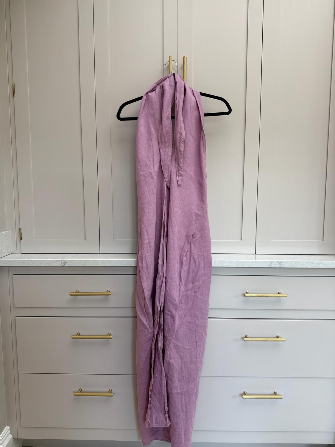 Long lilac garment hanging from a black hanger hooked onto the gold handle of a light-grey wardrobe with drawers and a marble worktop.