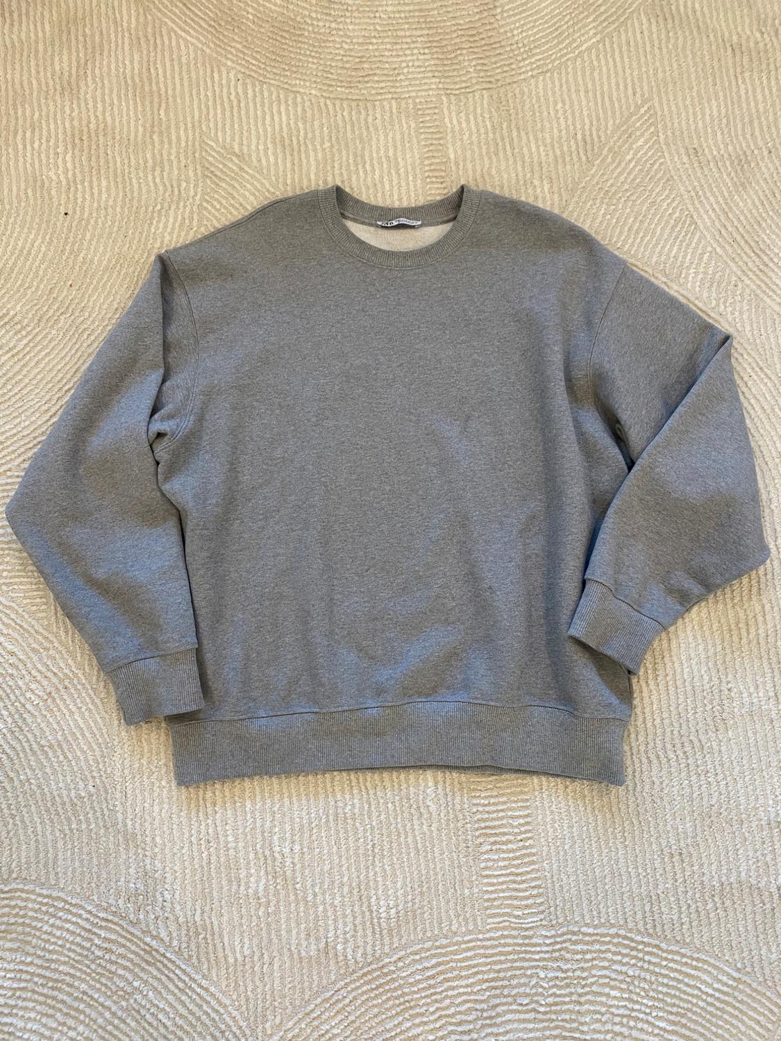 Gray long-sleeved crewneck sweatshirt on a beige rug with a circle design.