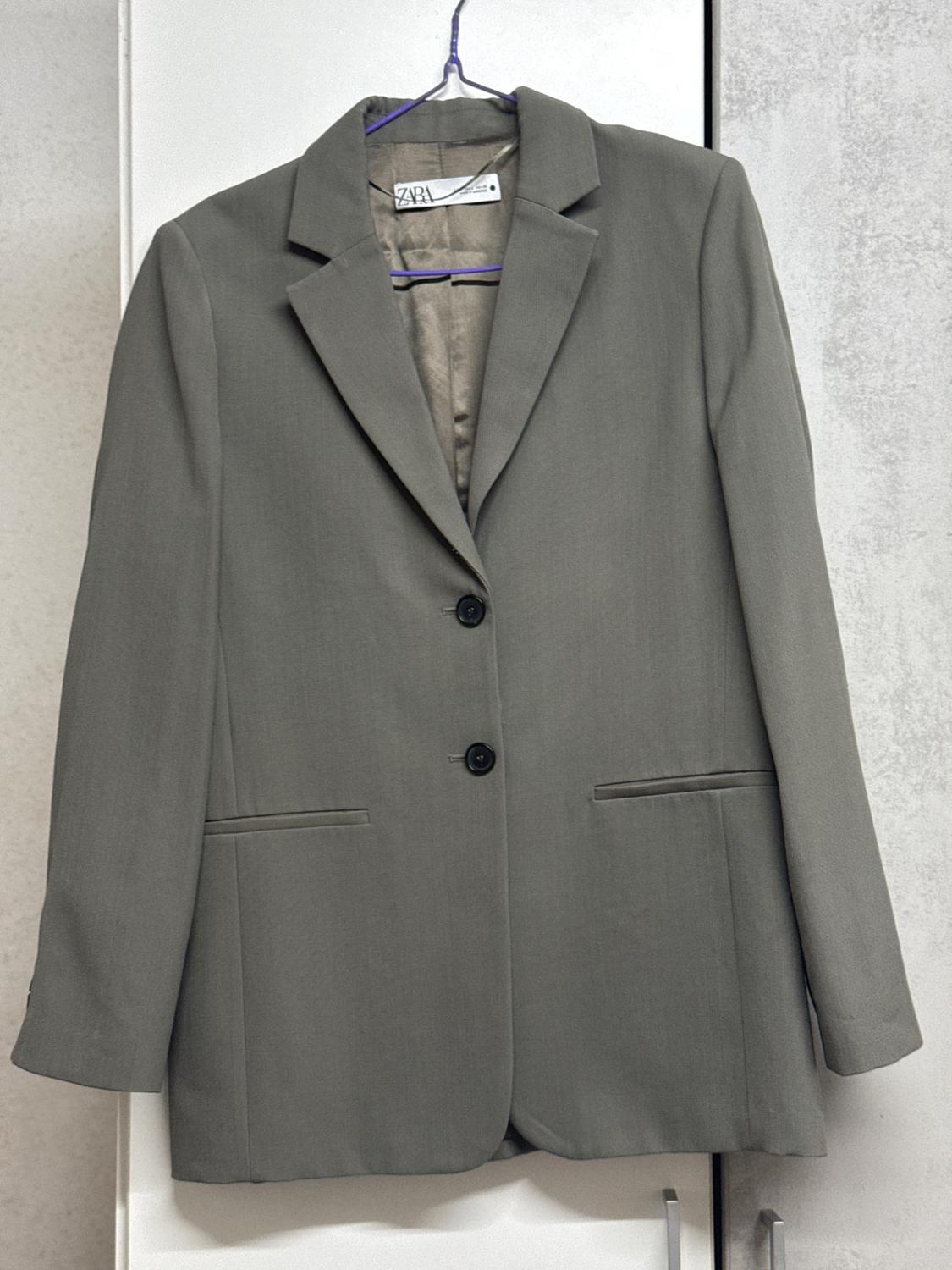 Two-button grey jacket hanging on a purple hanger, with a visible label inside, on a light background.