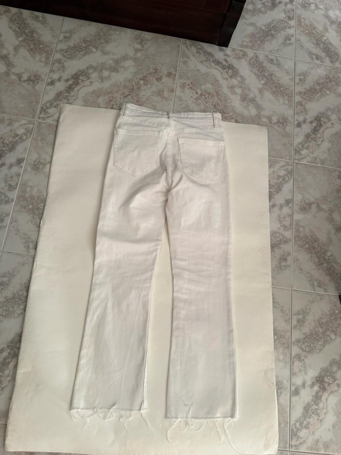 White jeans viewed from behind with a frayed hem, laid out on white paper on a tiled floor.