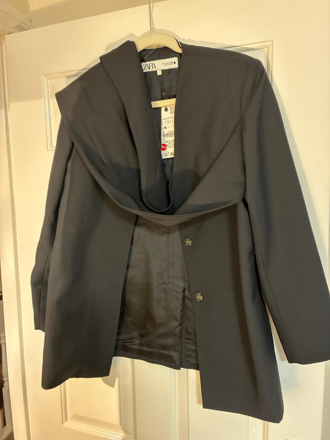 Black blazer with draped neckline hanging on a white door. Visible label with the text ZARA.