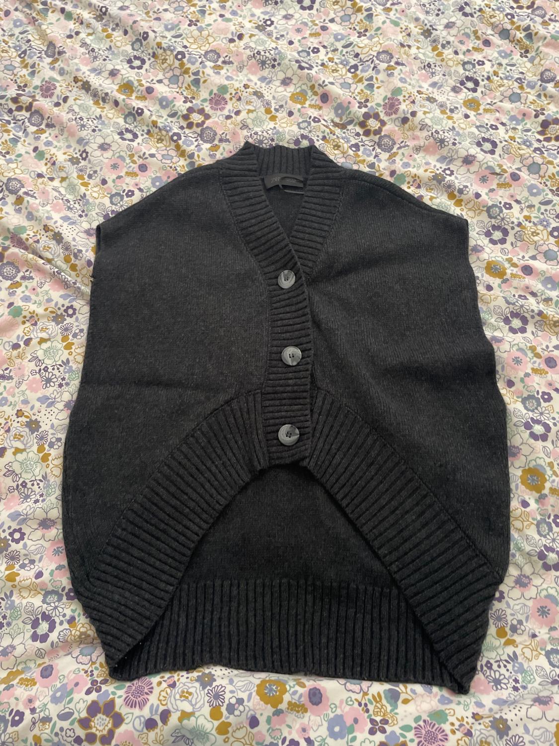 Black knitted waistcoat with large buttons over a floral quilt in pastel and purple tones.