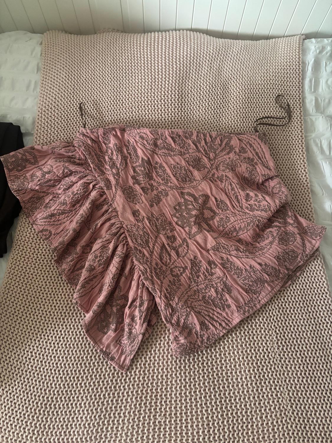 Pink crinkled fabric garment with a dark floral print and ruffles, laid out on a knitted throw on a bed.