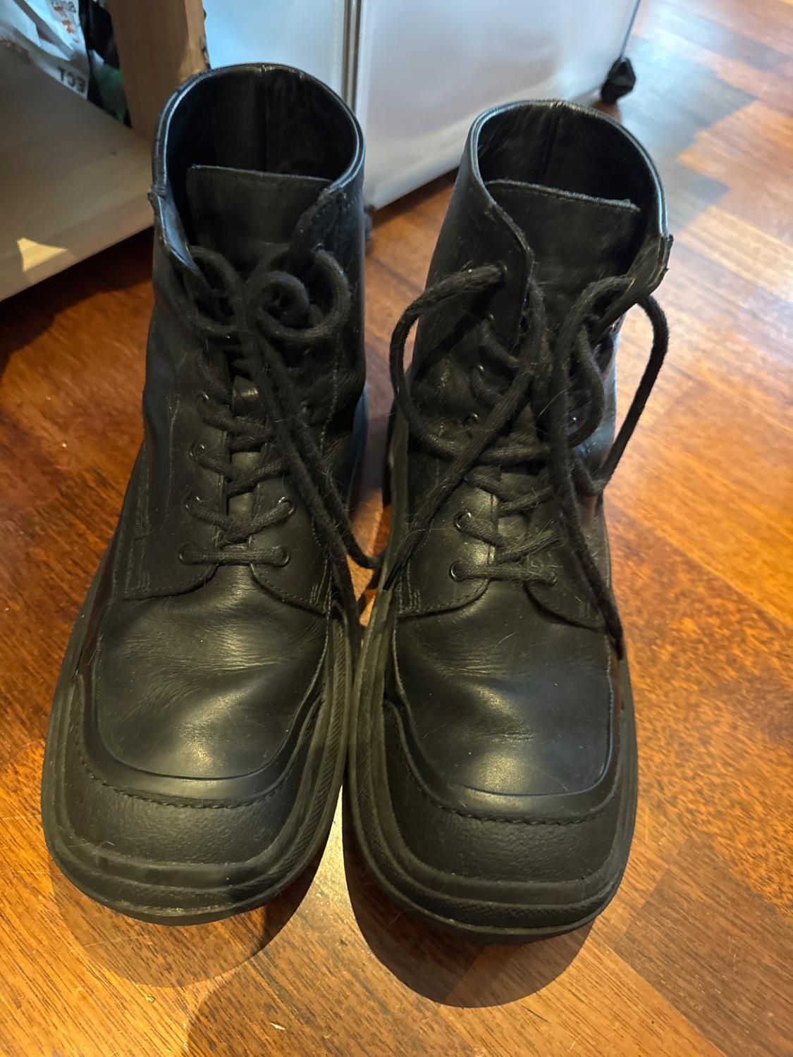 Pair of black leather boots with laces and round toes on a wooden floor.