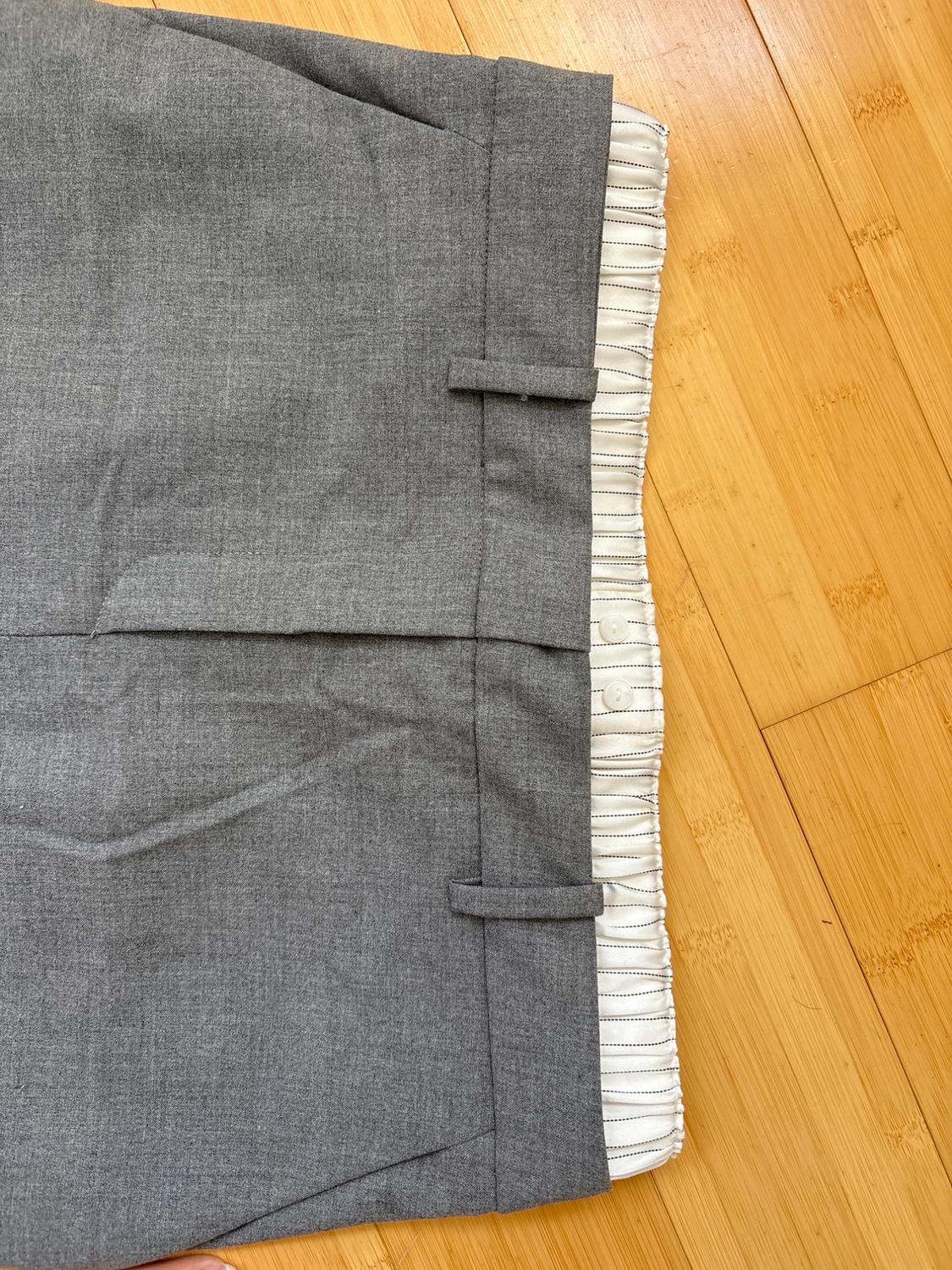 Gray pants with a white elastic waistband and black stripes, on a light wood floor. Detail of belt loops and visible seams.