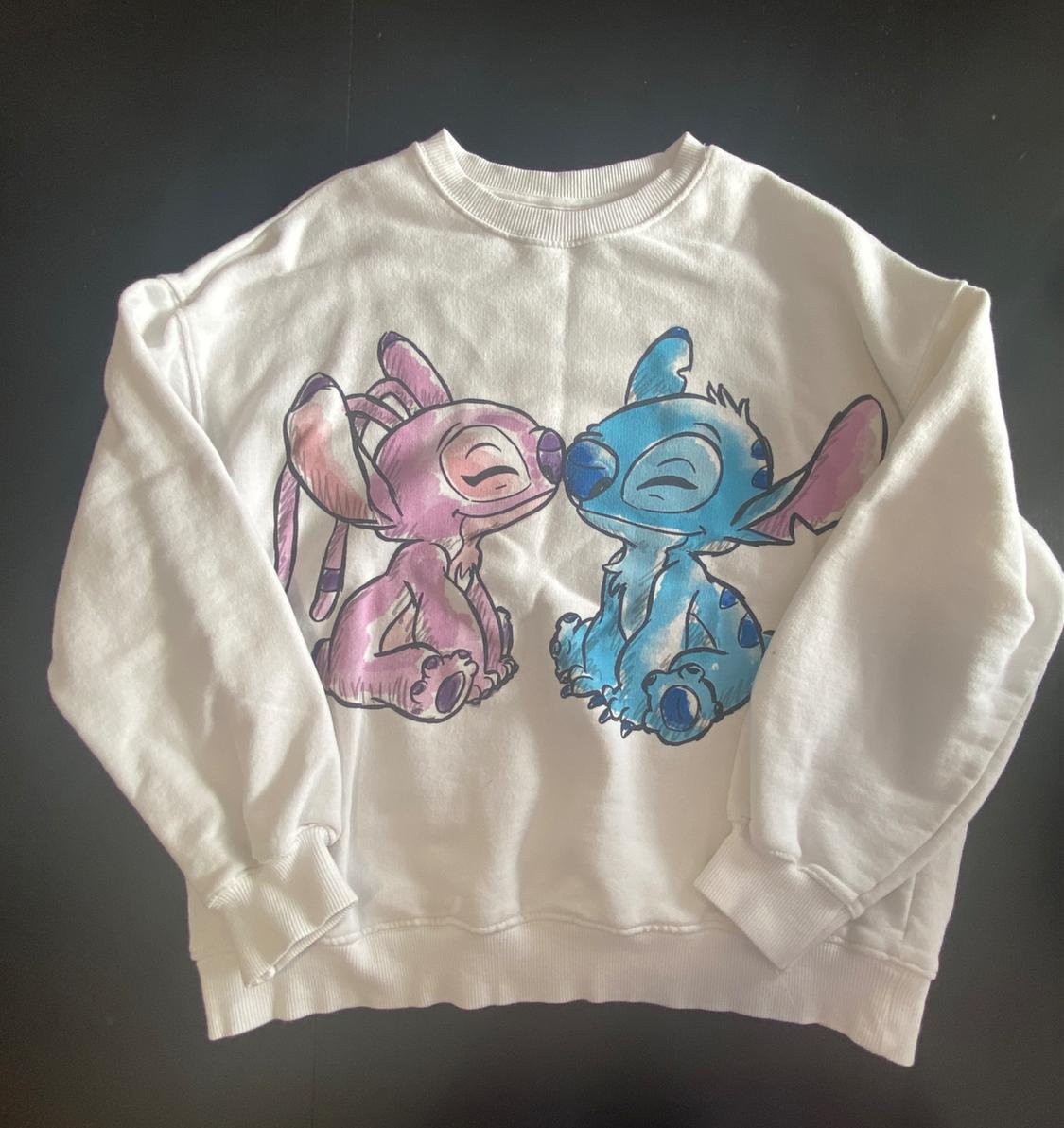 White sweatshirt with an illustration of two animated characters, one pink and one blue, sitting and smiling, on a dark background.