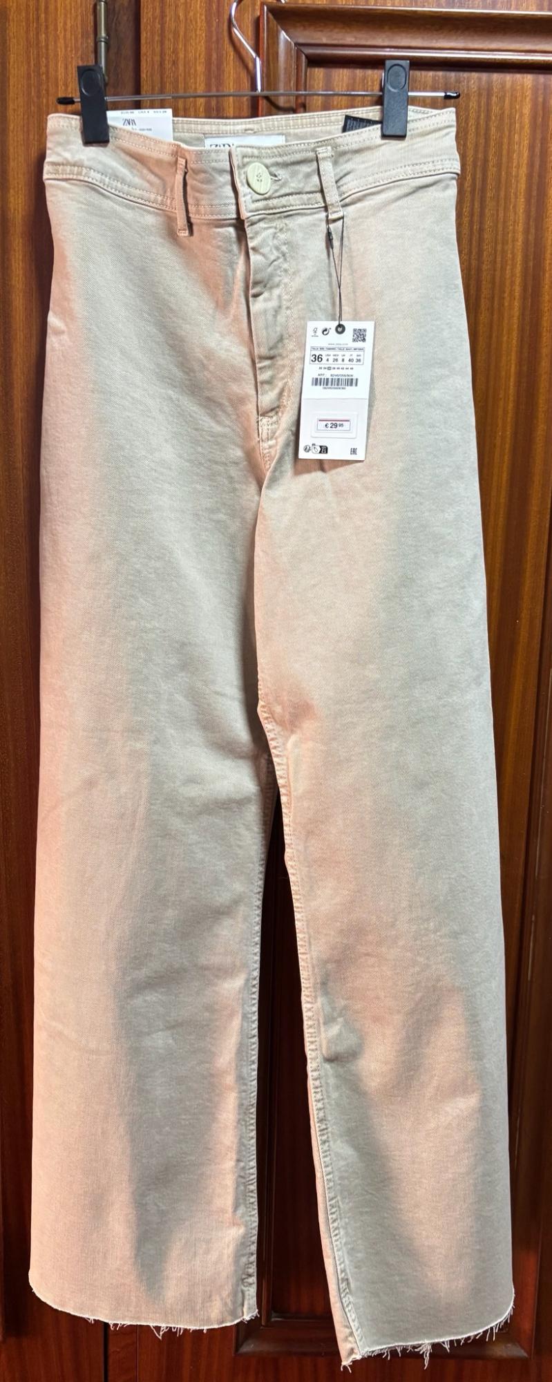 Μπεζ τζιν παντελόνι της μάρκας Zara κρεμασμένο σε κρεμάστρα πάνω από μια ξύλινη πόρτα, με ετικέτα τιμής 29,95 ευρώ.