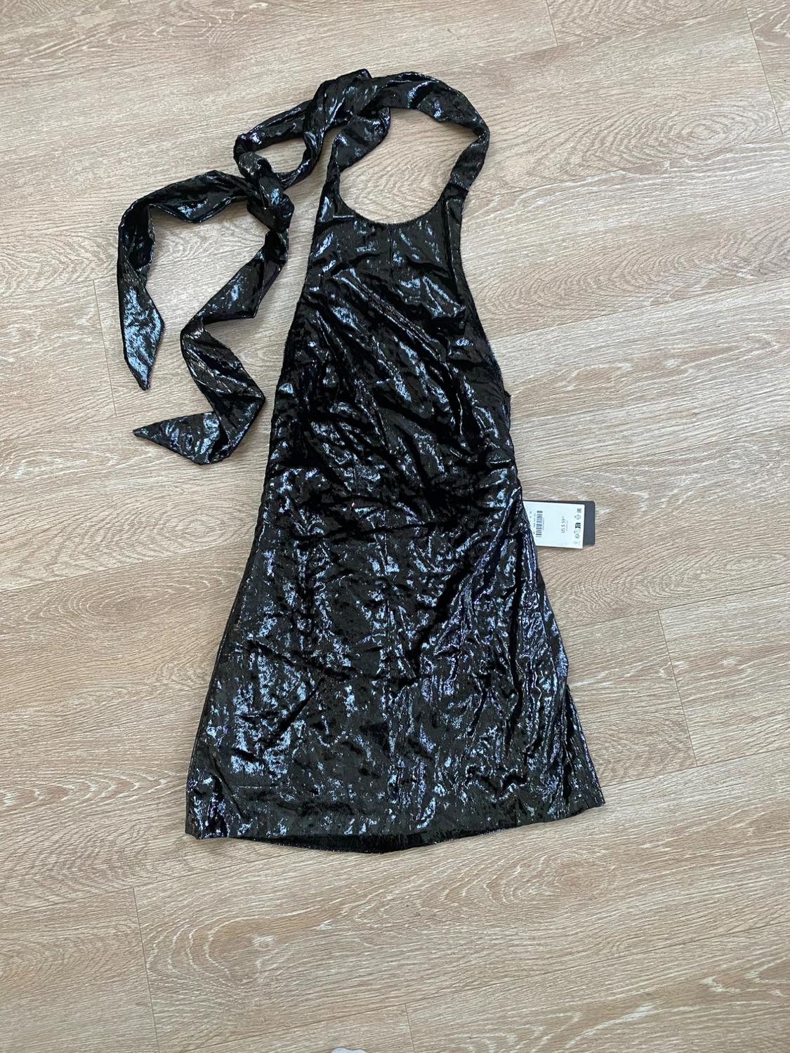 Shiny black dress with wide straps and a bow at the neck, on a light wood floor. Visible tag on the side.