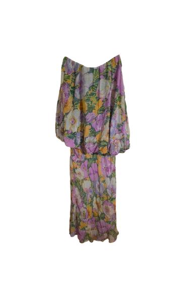 Long dress with a floral print in shades of purple, yellow, and green, featuring puff sleeves and a flowing skirt.