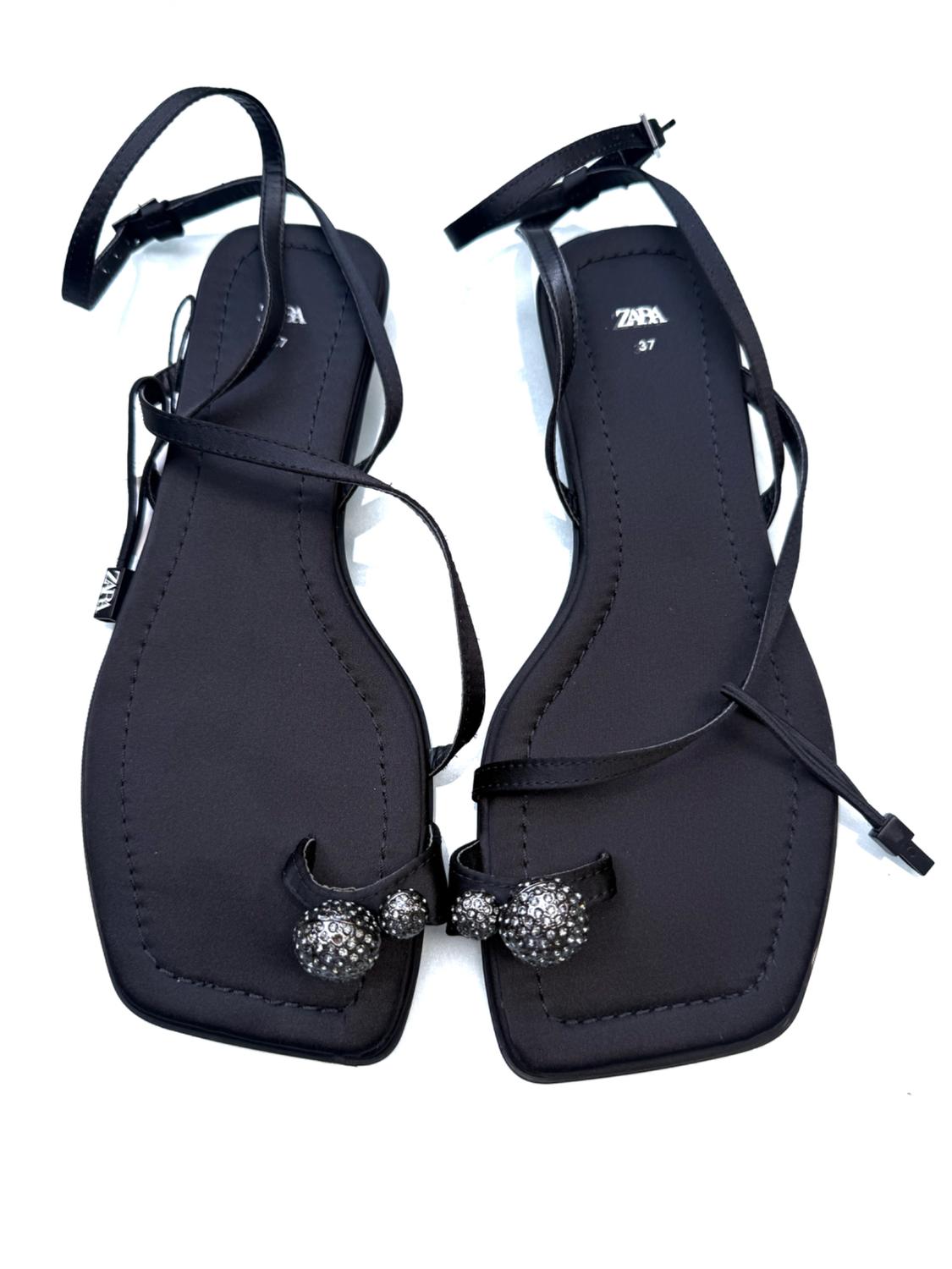 Black flat sandals with thin straps and sparkly embellishments at the front. Visible text: "ZARA 37".