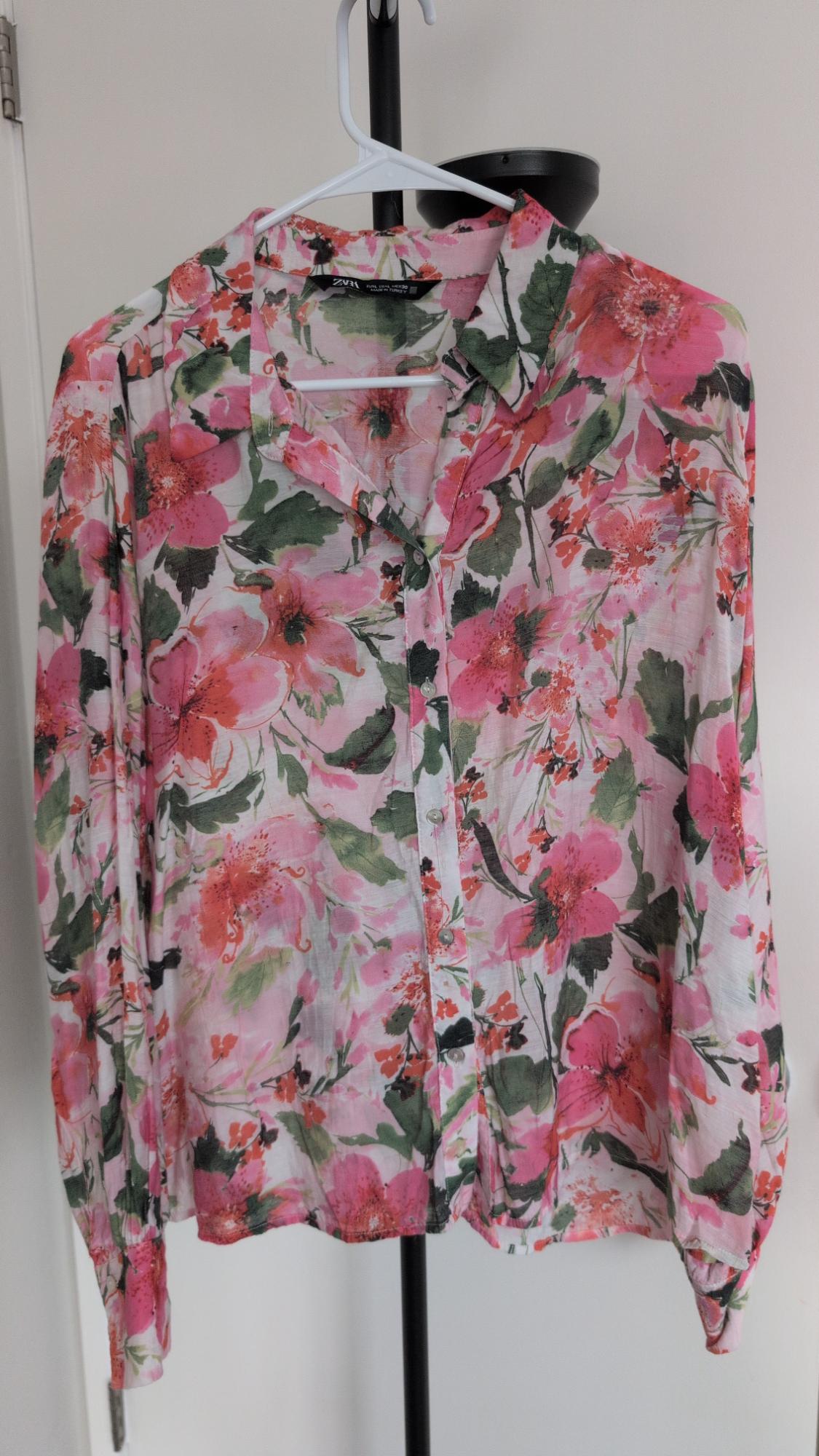 Pink and green floral print long-sleeved button-down shirt, hanging on a white hanger. ZARA is written on the tag.