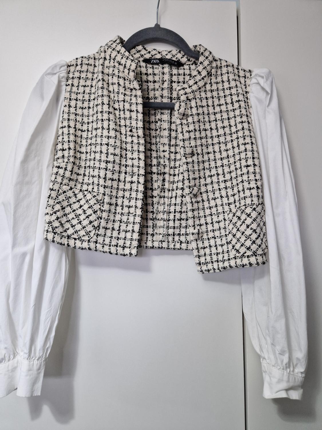 Fabric waistcoat with a black and white checked pattern over a long-sleeved white shirt, hanging on a black hanger.