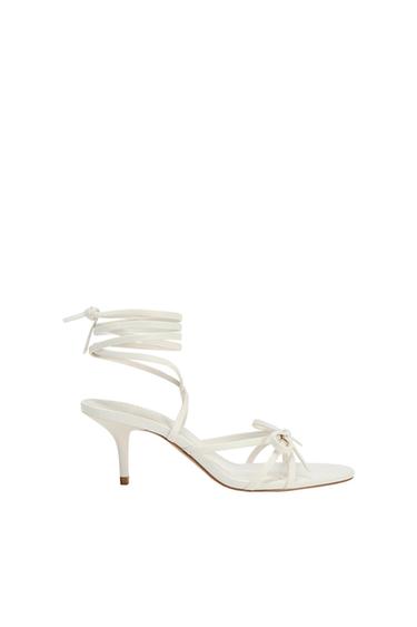 White low-heeled sandal with thin straps and ankle-tie closure, on a white background.