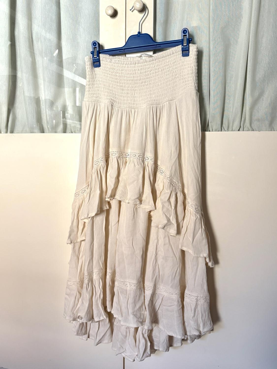 Long cream-coloured skirt with an elasticated waist, tiered ruffles and lace, hanging on a blue hanger in front of a white wardrobe.