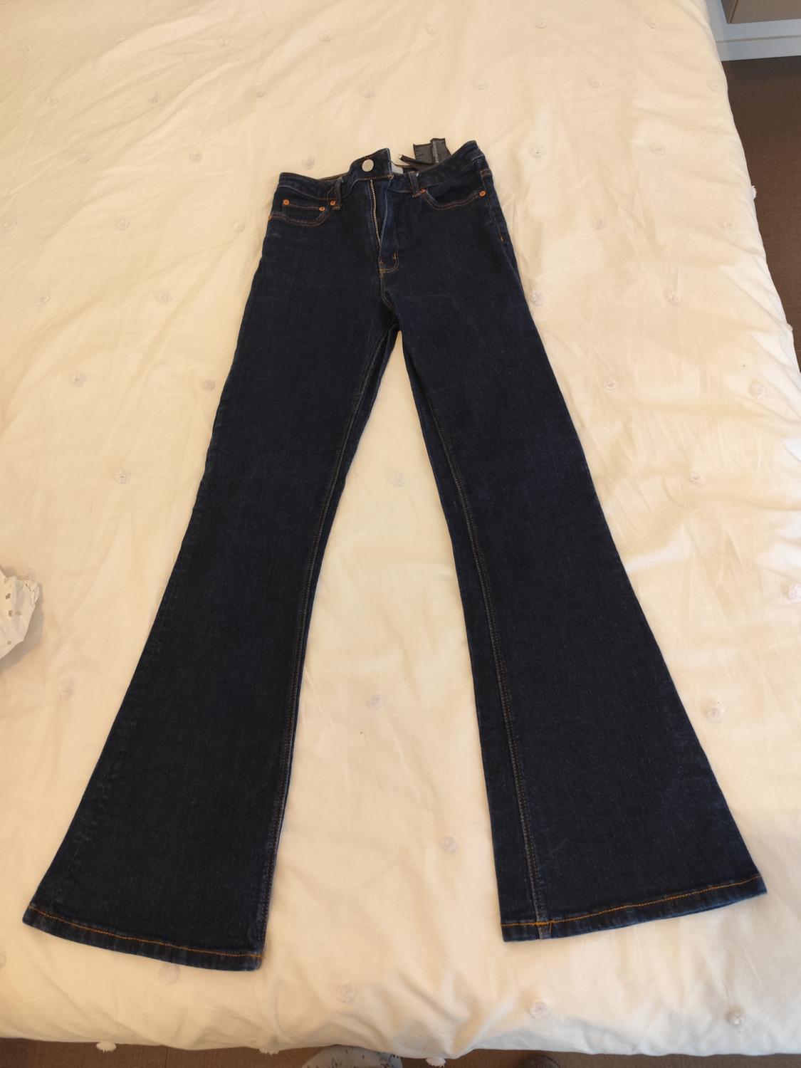 Dark denim flared jeans placed on a white bed with visible stitching details.