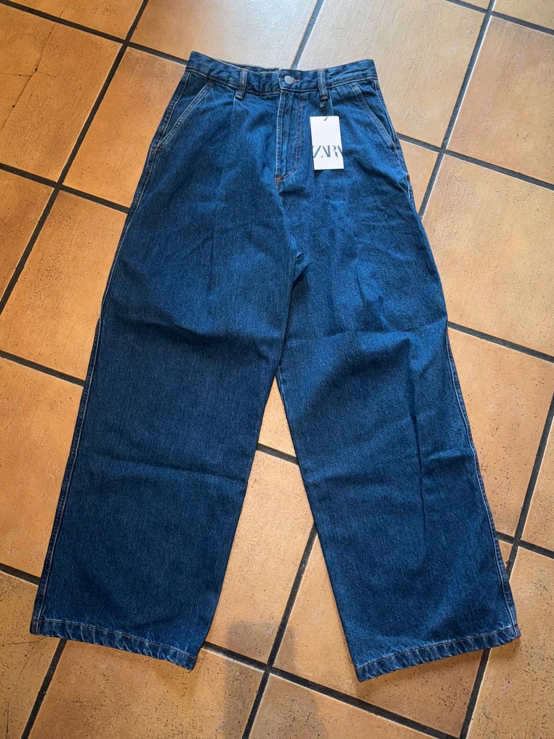 Blue wide-leg jeans with visible label on brown tiled floor.