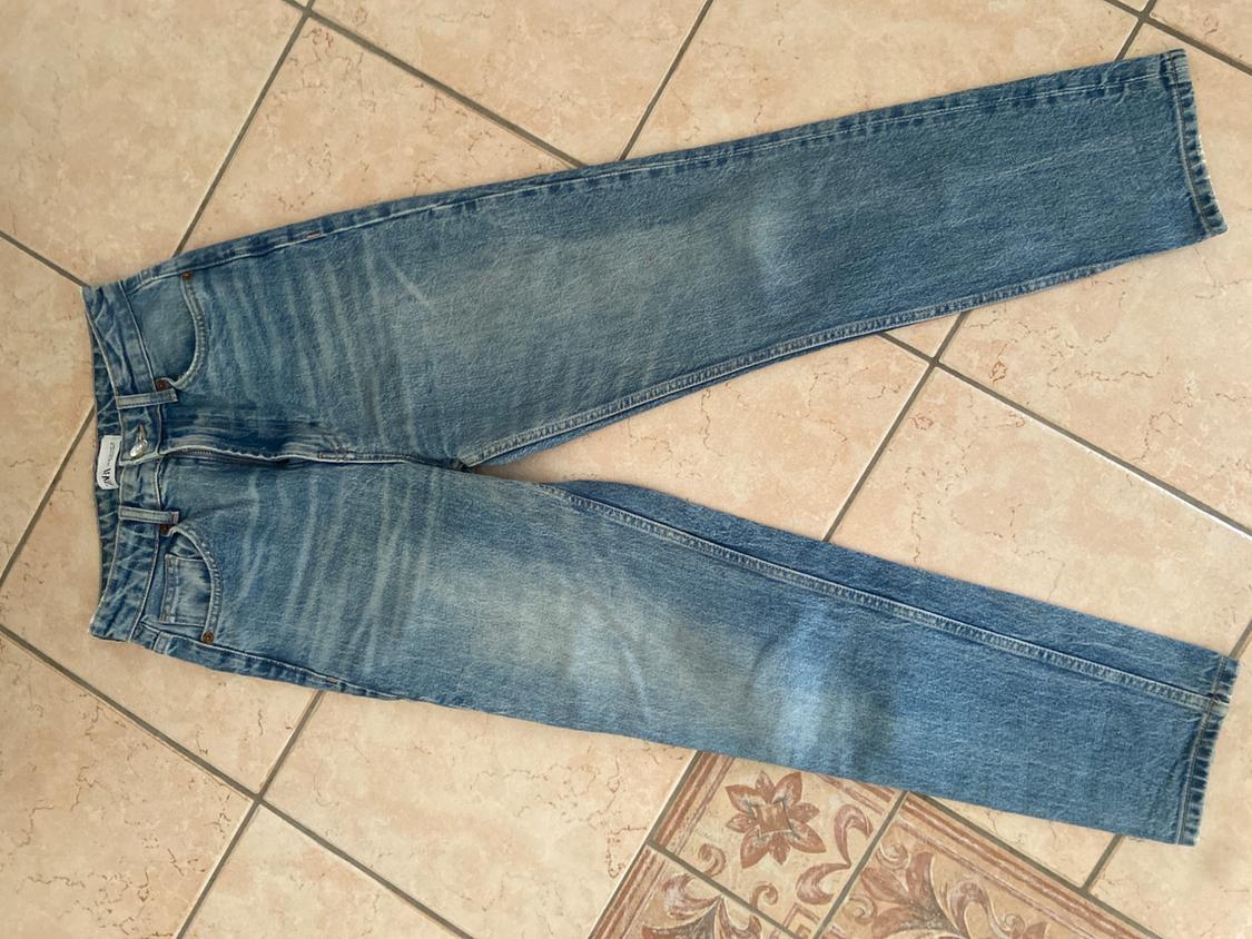 Worn blue jeans laid out on a beige tiled floor, showcasing a casual and relaxed style.