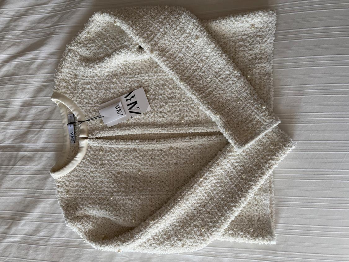 Cream textured jacket with small pearls, visible label with the text "ZARA", on a white surface.
