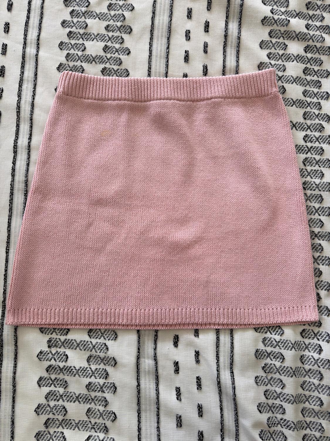 Light pink knitted miniskirt on a white fabric with black geometric patterns. Relaxed-style flat lay.