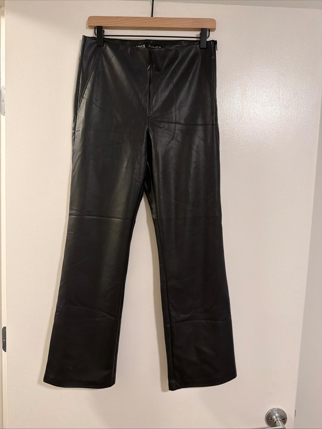 Black, straight-leg trousers hanging on a wooden hanger on a white door with a silver knob.