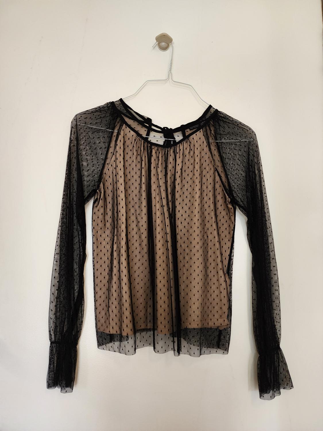Front view of a black sheer polka dot blouse with long bell sleeves.