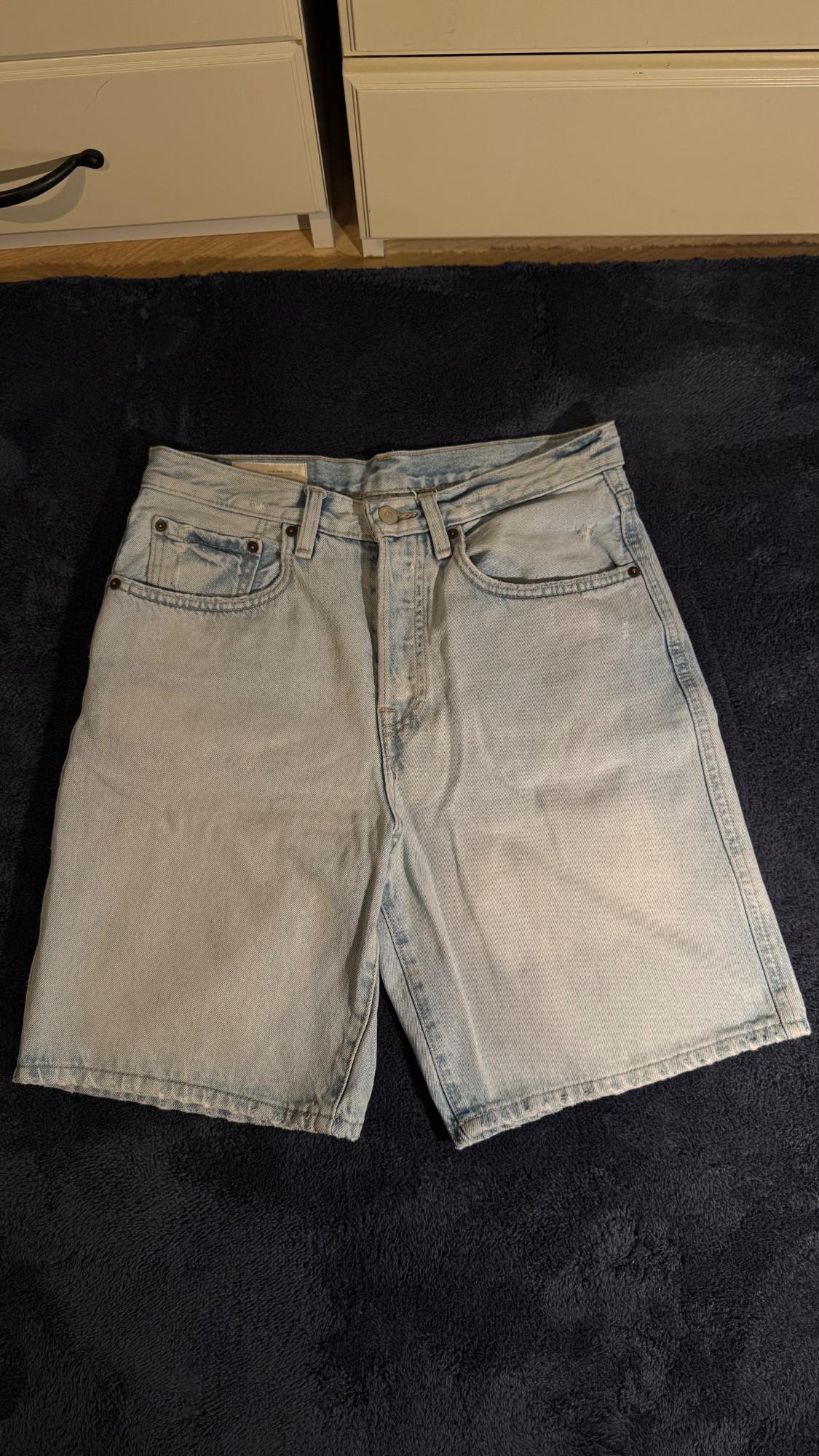 Light blue denim shorts on a dark blue surface. White drawers can be seen in the background.