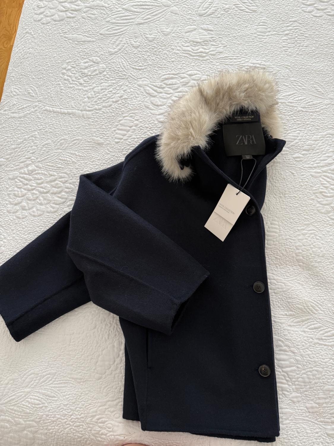 Navy blue coat with a fur collar on a white textured bedspread. Includes labels with the text ZARA and WOOL COLLECTION.